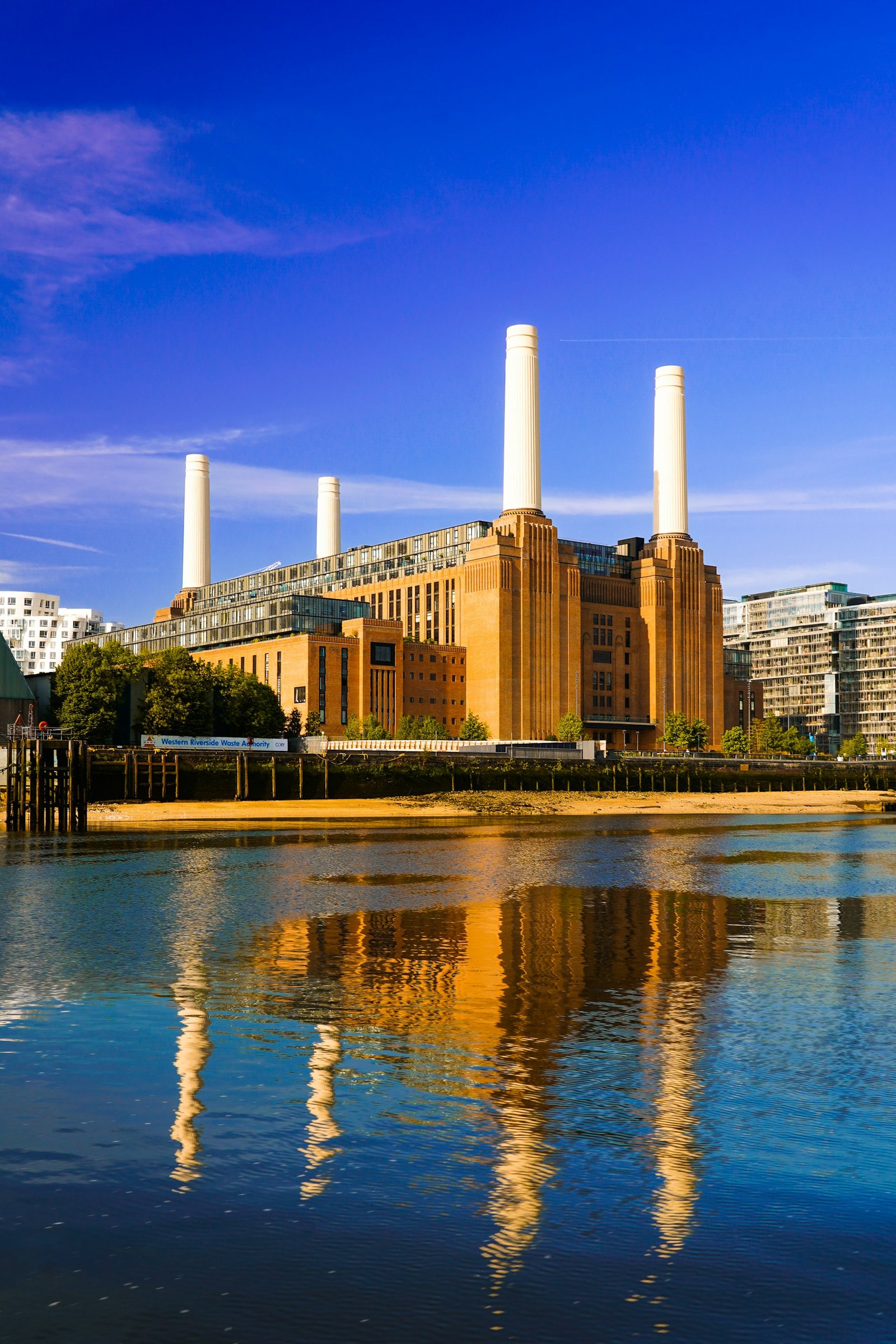 Battersea Power Station and its white chimneys beside the Thames under a blue sky.